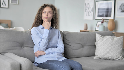 Pensive Curly Hair Woman Thinking while Sitting on Couch