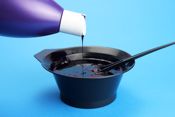 Pours hair dye from a bottle into a bowl