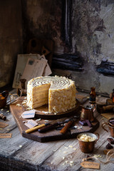 traditional hungarian cut esterhazy cake on wooden boards on grey wooden table with copper cups, vintage forks, almond flakes opposite concrete wall
