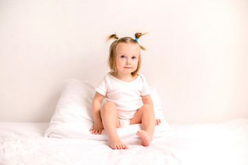 baby girl smiling in white clothes lying on a bed with white linens