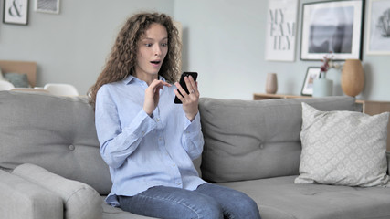 Obraz premium Relaxing Curly Hair Woman Cheering Success on Smartphone