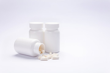 Three jars with medicines and scattered pills on a white background