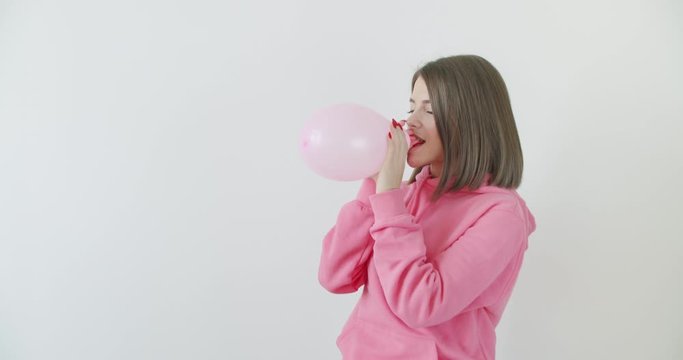 Young woman blowing a pink balloon