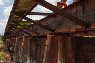 Rusting low train trestle with outrigger walkway outside a  derelict manufacturing facility, horizontal aspect