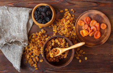 Dry fruits of dried apricots, raisins and prunes in wooden cups on rustic table, top view