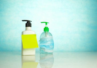 Hand sanitizers side by side where one is covered by face mask over blue background. Conceptual of keeping sanitized hands and wearing face mask. Selective focus.