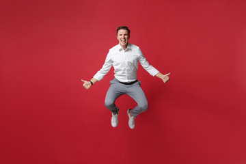 Fototapeta na wymiar Crazy young business man in white shirt, gray pants posing isolated on bright red background studio portrait. Achievement career wealth business concept. Mock up copy space. Jumping showing thumbs up.