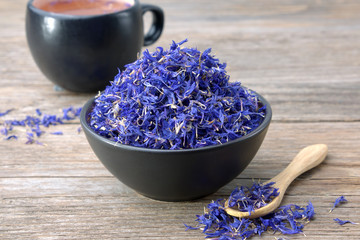Black ceramic bowl of dry blue cornflowers petals and herbal tea cup on table. Herbal medicine.