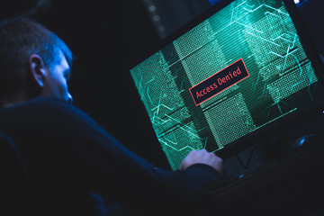 Caucasian man typing password on a computer in the dark, access denied seen on a monitor 