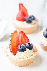 Cakes with fresh berries. Cream tartlet with strawberries and blueberries