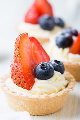 Cakes with fresh berries. Cream tartlet with strawberries and blueberries