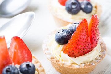 Cakes with fresh berries. Cream tartlet with strawberries and blueberries