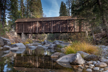 Fototapeta na wymiar A view of Yosemite Wawona covered Bridge over the Merced River by Mariposa, in the fall, featuring yellow colors, and blue sky California, USA 