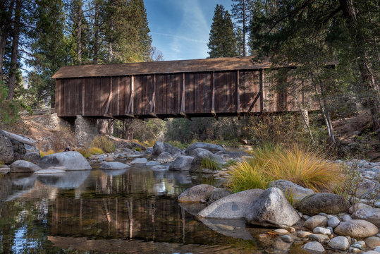 A view of  Yosemite Wawona covered Bridge over the Merced  River by Mariposa, in the fall, featuring yellow colors, and blue sky California, USA 