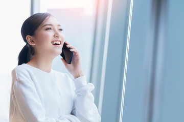 entrepreneur  startup business owner attractive asian female business woman communication with smartphone and laptop white dress cheerful and smile with confience blur office background
