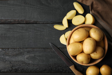 Bowl with young potato, towel and knife on wooden background, top view