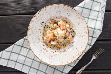 Gnocchi with bacon, tomatoes and parmesan cheese on white plate on black wooden table