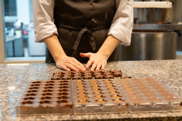 Fototapeta premium Pastry chef processing chocolate in kitchen. Selective focus of hands and pralines, filling chocolate mold. Liquid chocolate from top view
