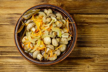 Delicious marinated mushrooms with carrot, onion and spices in ceramic bowl on wooden table. Top view