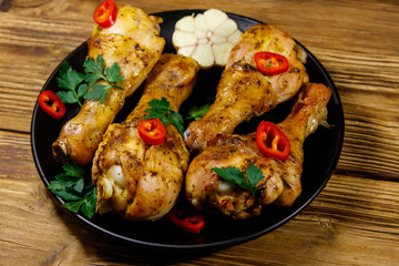Roasted chicken drumsticks with spices in a black plate on a wooden table
