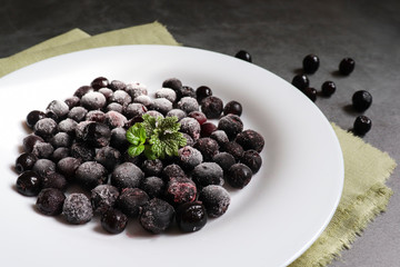 Frozen black rowan berries on a white plate and cement background. The concept of the use and preservation of frozen foods.