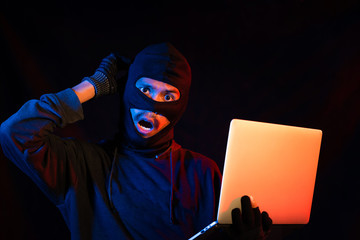 The thief holds the computer on a black background,Wondering face