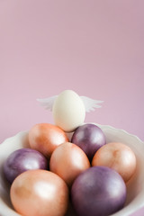 White chicken egg with wings on top of other colored eggs. Creative Easter concept. Copy space for text.
