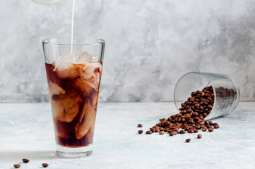 Milk Being Poured into Iced Coffee in Tall Glass on Light Grey Background. Concept Refreshing...