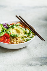 Quinoa salad with broccoli, tomatoes and avocado in white bowl.