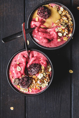 Vegan berry smoothie bowl with tahini and muesli, dark background, top view. Homemade berry ice cream with peanut butter and granola.