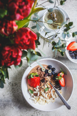 Flat lay of beautiful breakfast with granola, berries, tea and a bouquet of flowers.