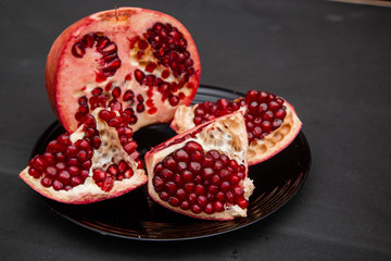Fresh grenades cut in half with half broken into pieces lie on a plate that stands on a black table.