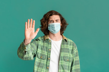 Epidemic outbreak. Young guy wearing mask and showing STOP gesture on turquoise background