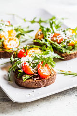 Tomatoes, arugula and cheese sandwiches on a gray plate.
