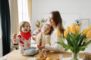 Friendly young family having good time together in a bright kitchen. Little baby girl on the table near tulips playing with a spoon.