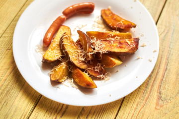 Fried crispy potato with cheese and sausages on a white plate on a wooden background.
