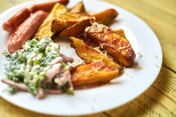 Fried crispy potato with cheese, sausages and salad on a white plate on a wooden background.