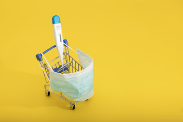thermometer in a shopping cart and medical masks on a yellow background. Health and vitamin...