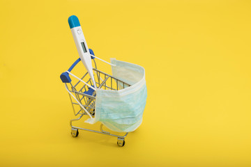 thermometer in a shopping cart and medical masks on a yellow background. Health and vitamin...
