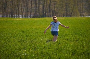 Young girl dancing happily in a luscious green grass meadow enjoying a warm day in spring.