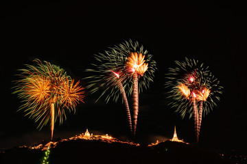 Abstract the colourful fireworks display is shot above the mountains and the golden pagoda of the temple at the annual fireworks festival in Phetchaburi, Thailand.