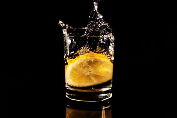 Splash in a glass with lemon on a black background. Fresh healthy drink concept