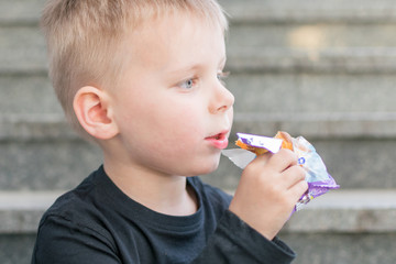 A little boy of 3-5 years eats on the street.