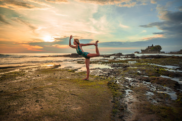 Outdoor sunset yoga. Attractive woman practicing yoga, standing in Natarajasana, Lord of the Dance Pose. Balancing, back bending asana. Bali, Indonesia