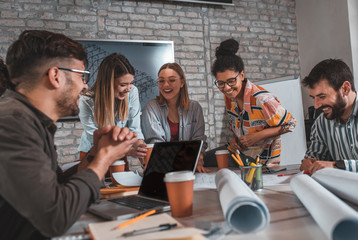 Group of modern business people in casual wear discussing architectural designs while sitting in the creative office.