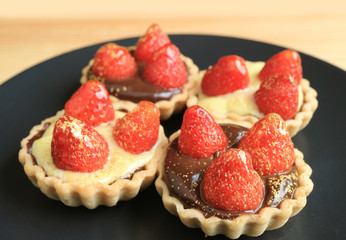 Four of tasty fresh strawberry tartlets on a black plate