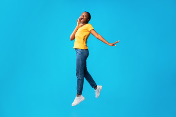 Fototapeta na wymiar Girl Jumping Shouting Holding Hand Near Mouth Over Blue Background