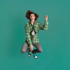 Happiness and freedom. Cheerful young guy in casual clothes jumping on turquoise background