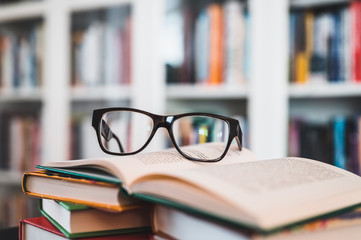Glasses on stack of books. Library in the background. Books and glasses.