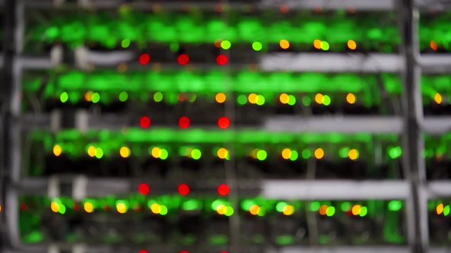 Large wired internet datacenter storage. ASIC miners on stand racks mine bitcoin in server room. Cryptocurrency mining equipment on large farm. Supercomputer blinking with lights. Defocus bokeh lights